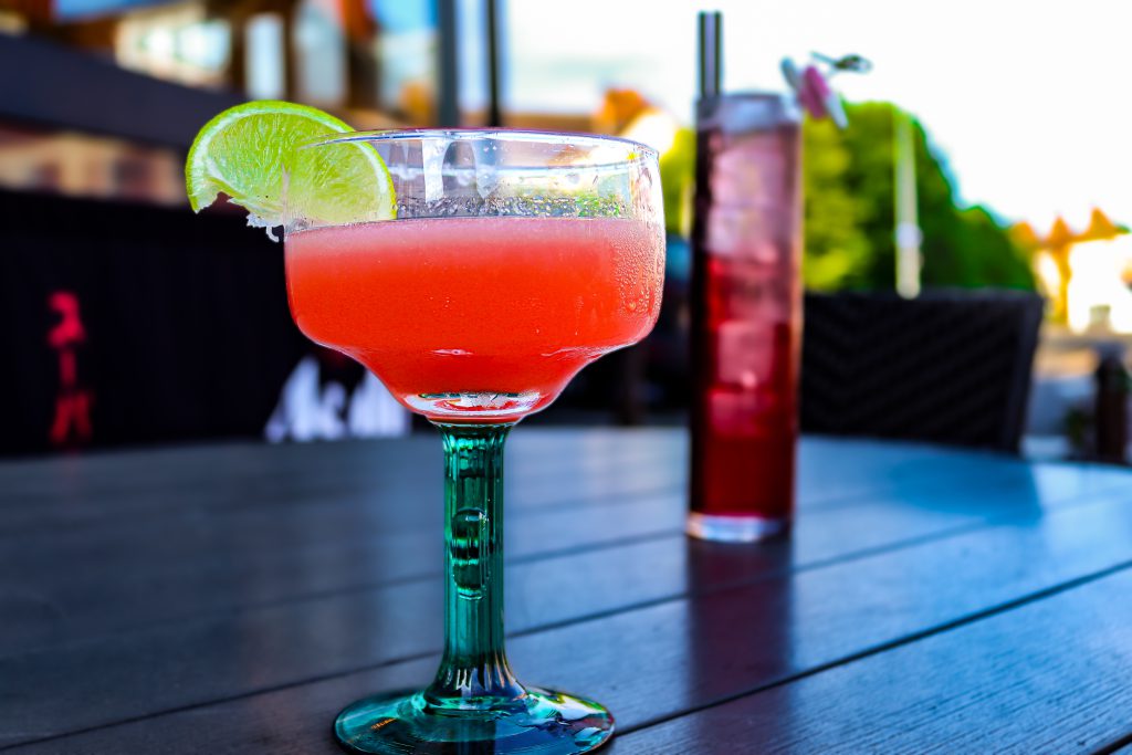 A refreshing pink cocktail garnished with a lime wedge, served on an outdoor table at Ascotts Restau.